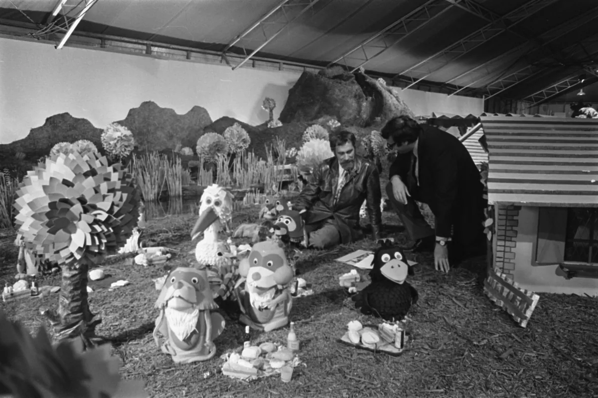 Zwart-witfoto uit 1970: de poppenset van Fabeltjesland met figuren uit De Fabeltjeskrant in een tent, met Thijs Chanowski en een medewerker tussen de poppen