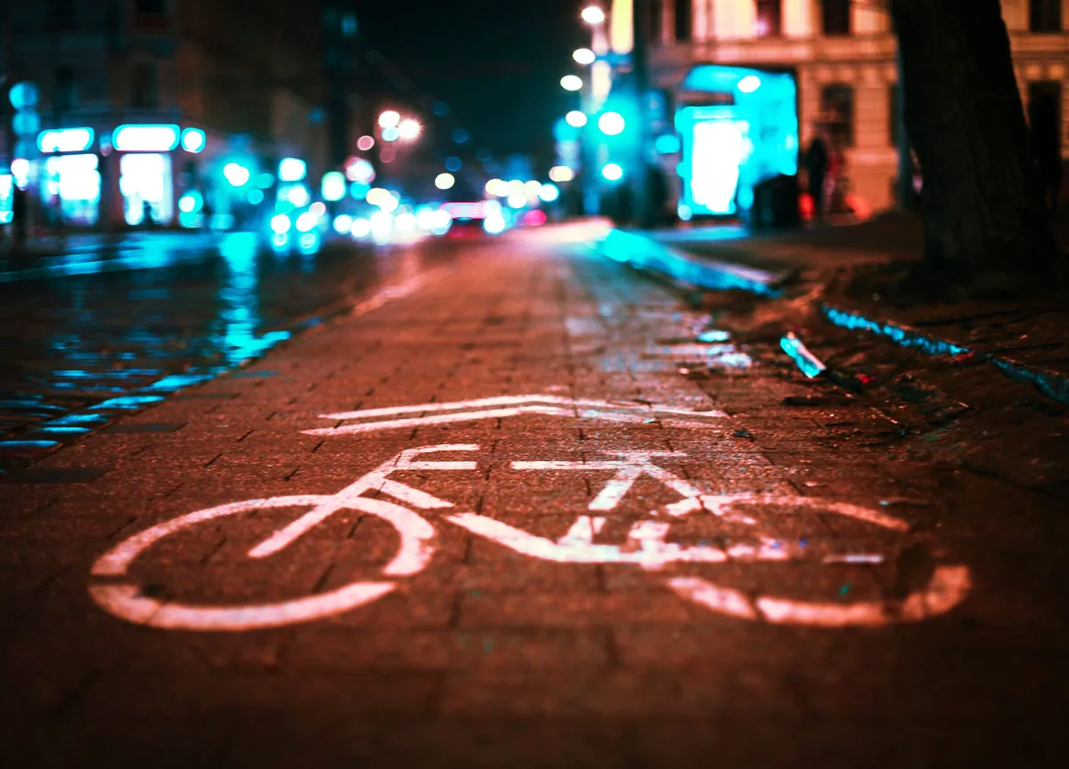 Fietspad met fietssymbool op het asfalt, verlicht door straatlantaarns en winkels in de avond