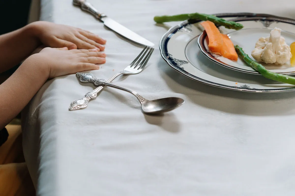 Kinderhanden aan tafel bij een bord met groenten