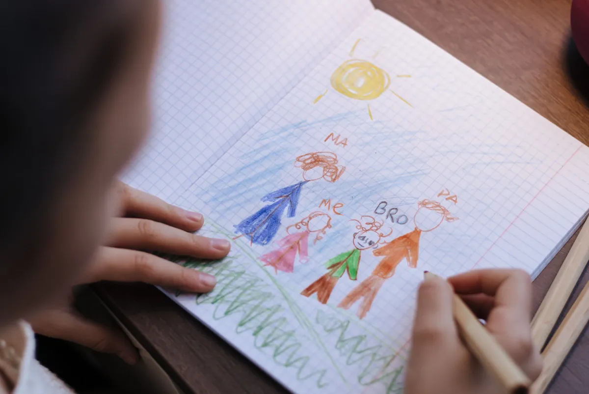 Kinderhanden tekenen met kleurpotloden een familie met een zon in een schrift