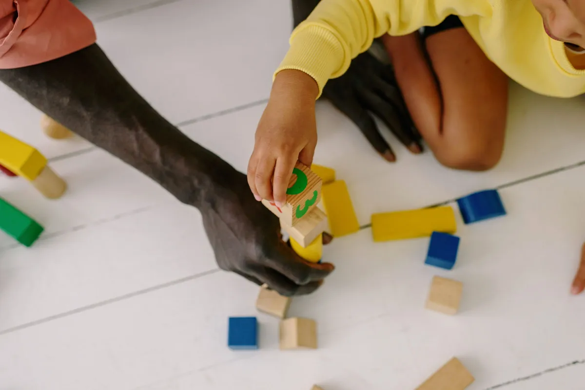 Kind en volwassene bouwen samen met gekleurde houten blokken op een witte vloer