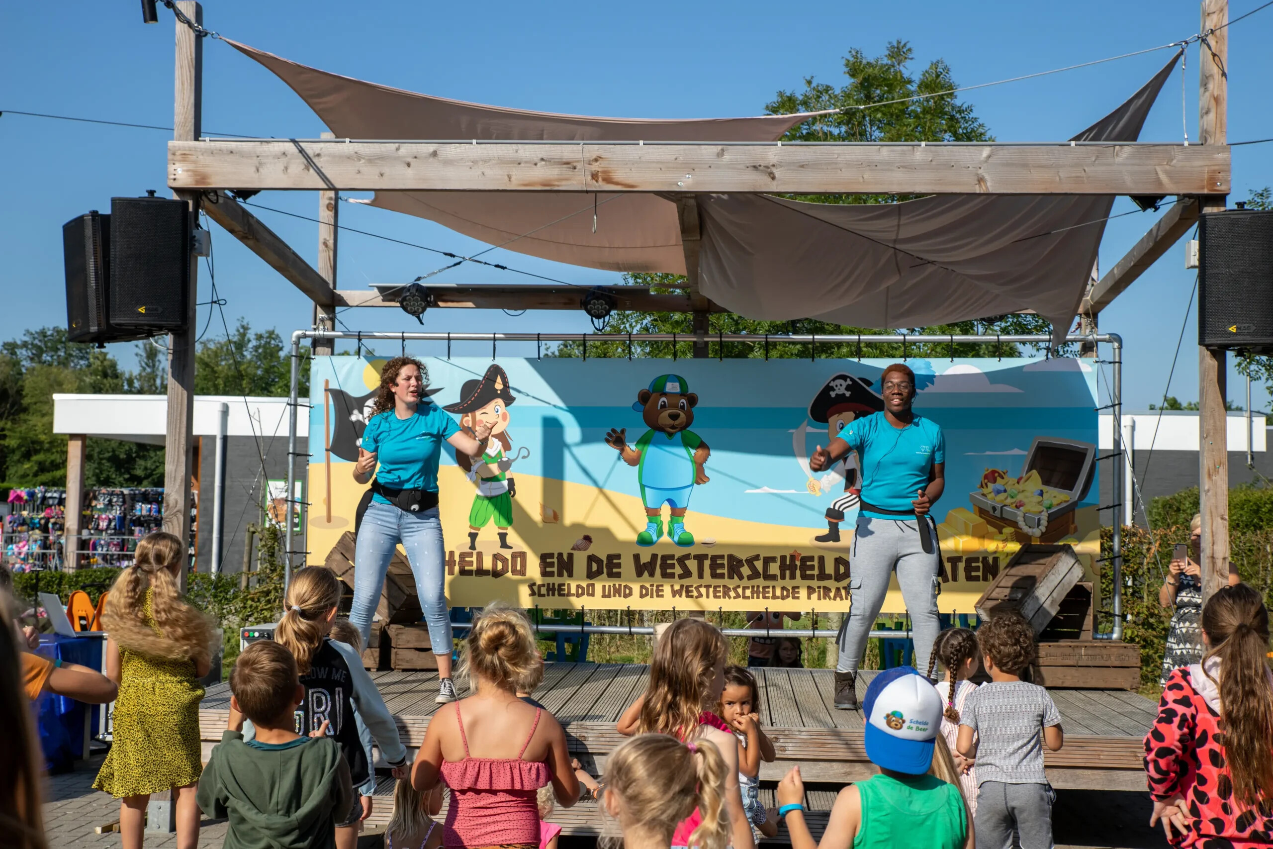 Twee artiesten dansen met kinderen op het buitenpodium tijdens de animatie op Camping Scheldeoord in Zeeland