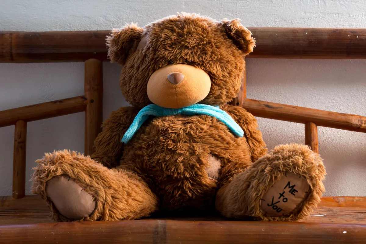 Bruine teddybeer met een blauwe sjaal op een houten bankje