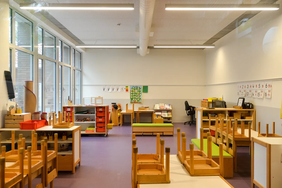 Licht klaslokaal van een basisschool met tafeltjes, kasten en een leeshoek
