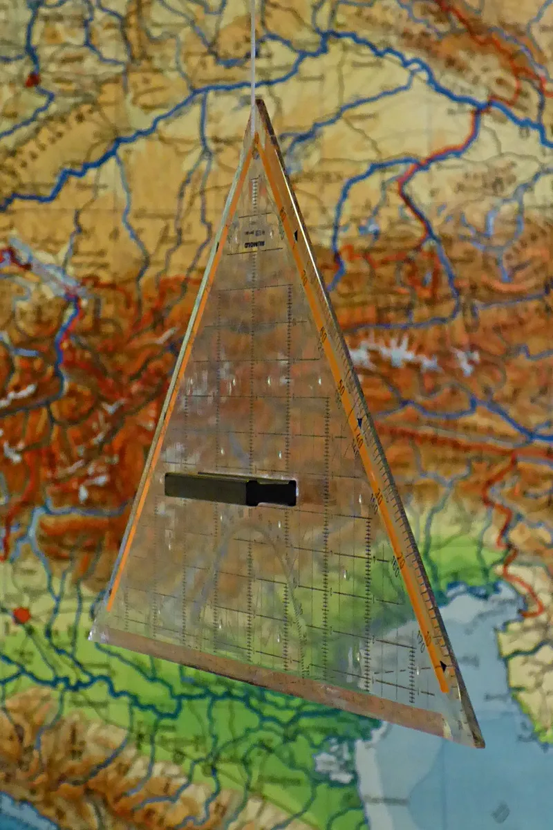 Een doorzichtige geodriehoek met gradenboog hangt voor een kleurrijke landkaart